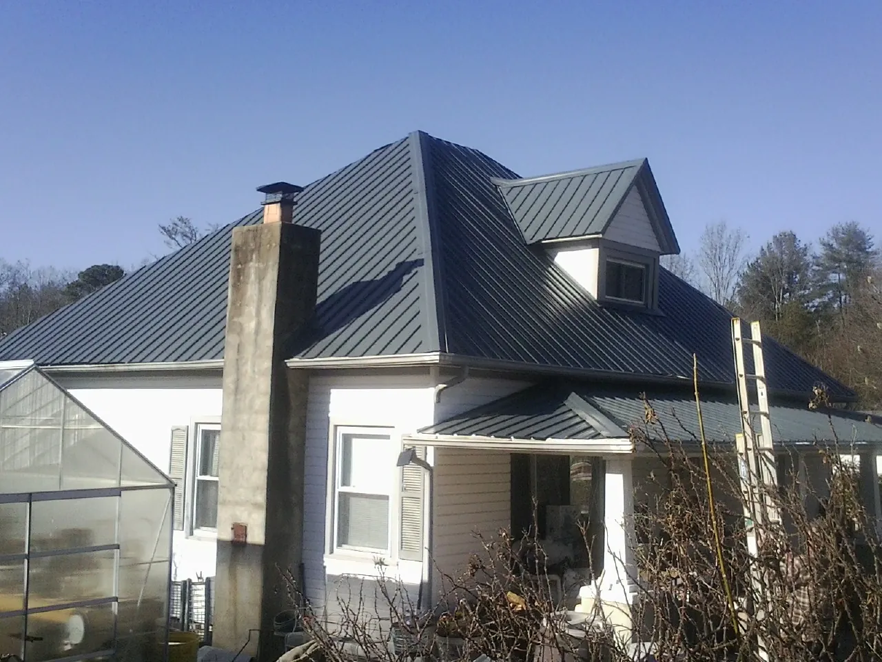 Dark blue standing seam metal roof on a white farmhouse with dormer in Richmond